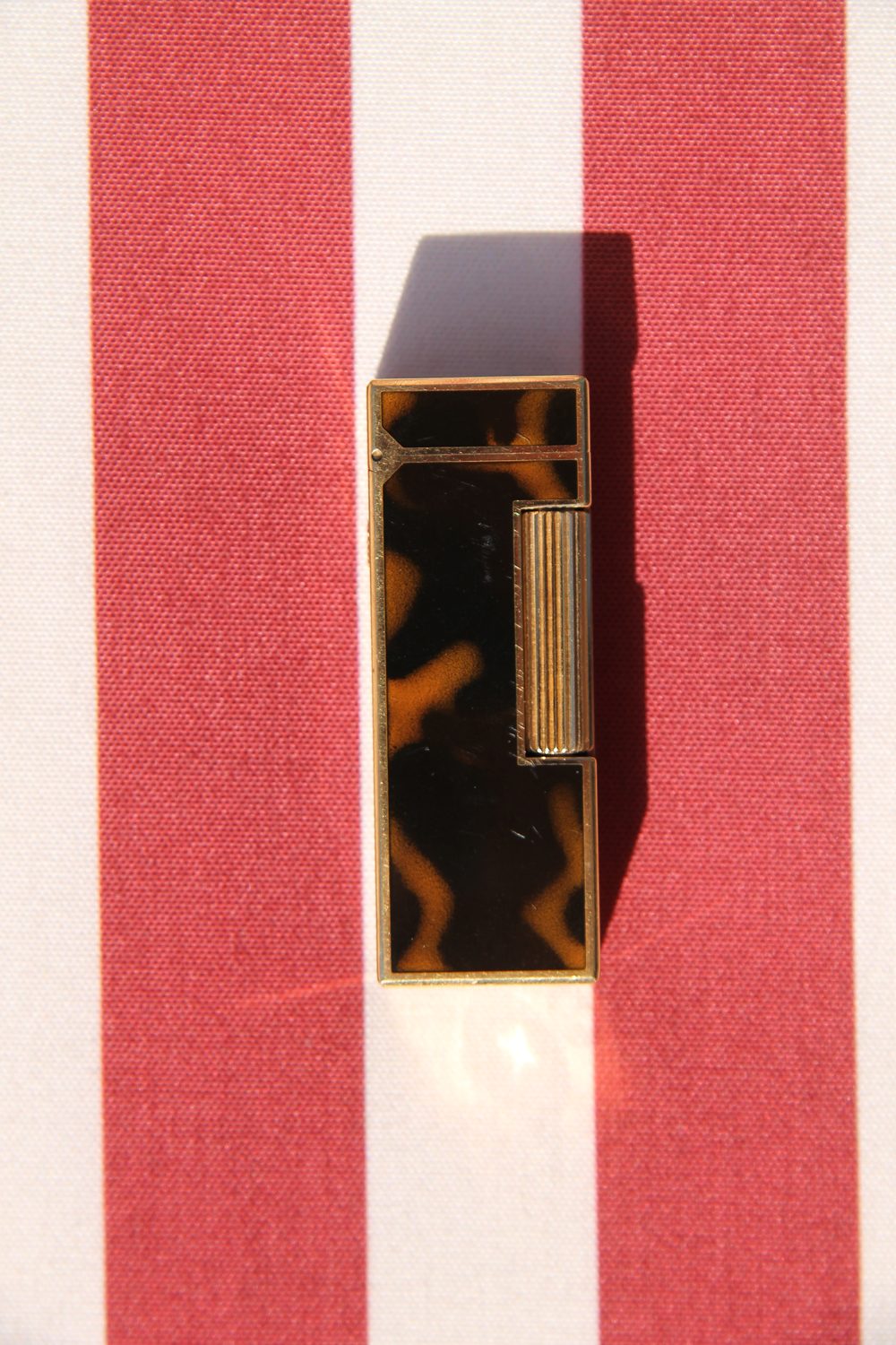 Dunhill Rollagas tortoiseshell lighter lying flat on a striped cloth, showing the ribbed roller