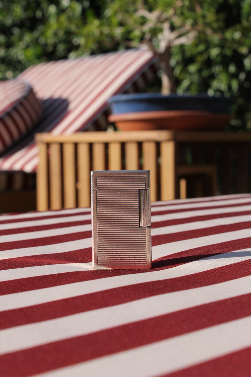S.T. Dupont Ligne 1 Grand silver lighter with fine horizontal lines standing on a striped cloth