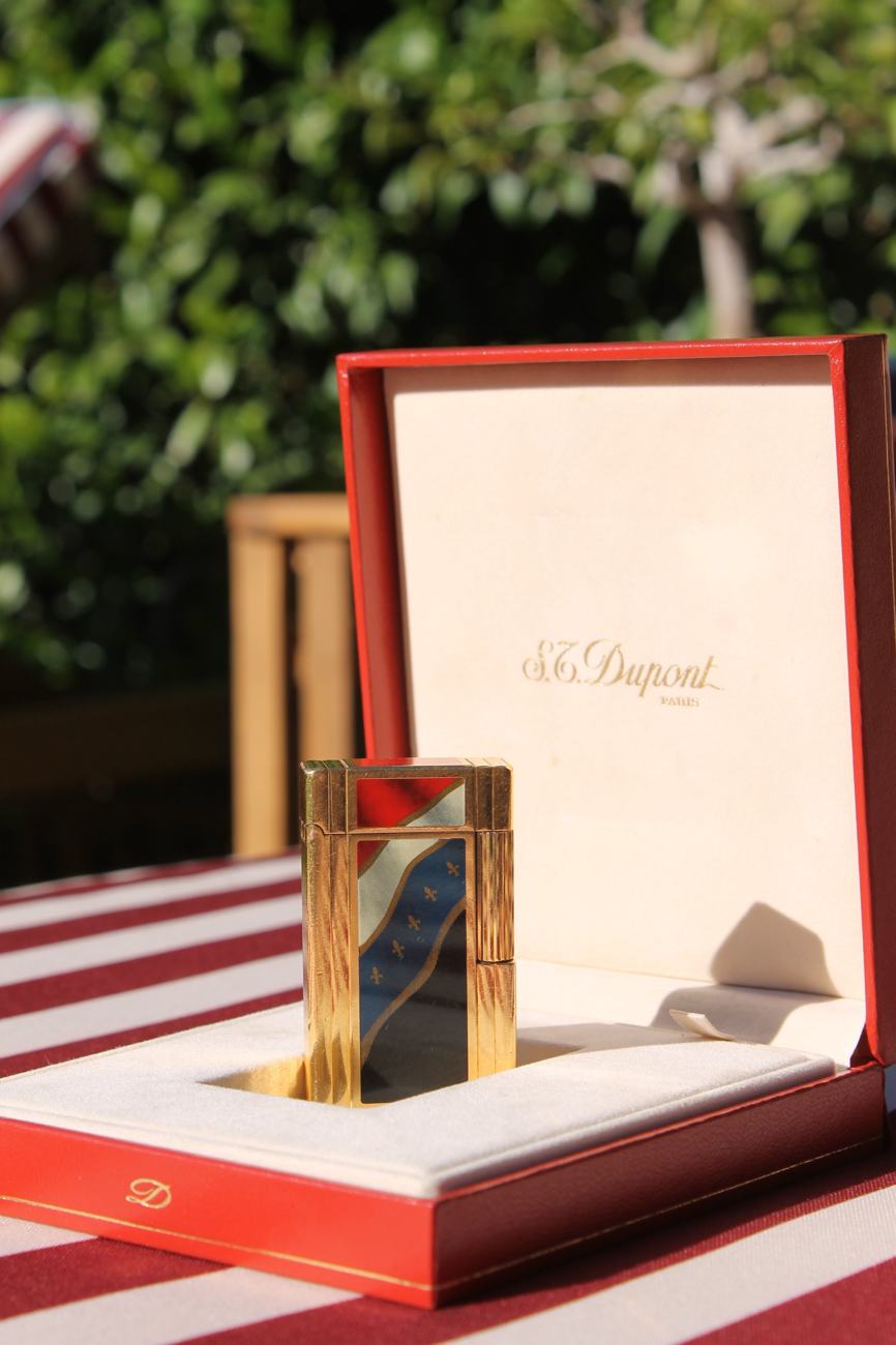 S.T. Dupont lacquered gold lighter standing in its open red presentation box, garden behind